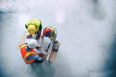 3 Männer mit Bauhelm über Plan gebeugt